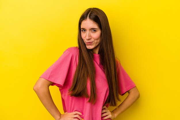 Young caucasian woman isolated on yellow background frowning face in displeasure, keeps arms folded.