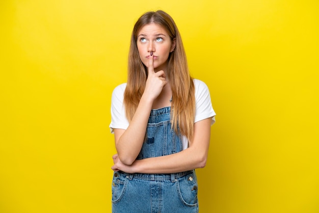 Young caucasian woman isolated on yellow background having doubts while looking up