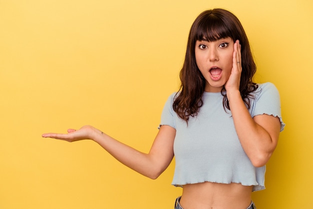 Young caucasian woman isolated on yellow background impressed holding copy space on palm.