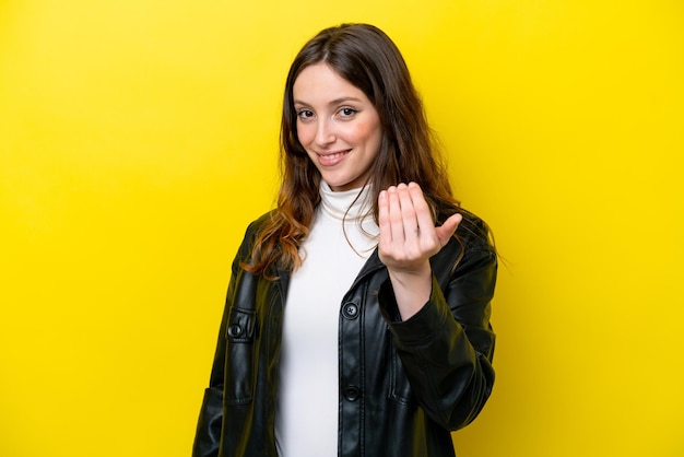 Young caucasian woman isolated on yellow background inviting to come with hand Happy that you came