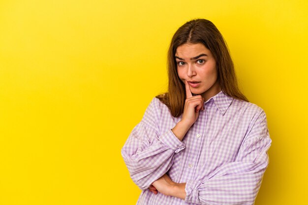 Young caucasian woman isolated on yellow background looking sideways with doubtful and skeptical expression.