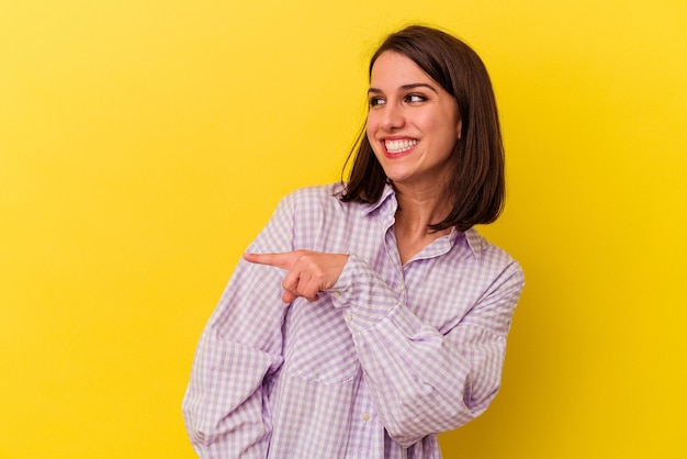 Young caucasian woman isolated on yellow background looks aside smiling cheerful and pleasant