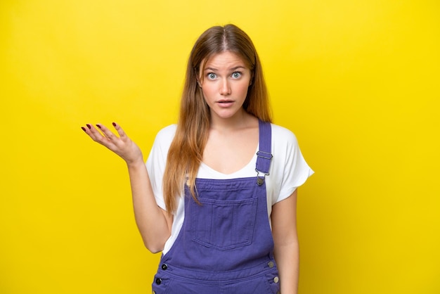 Young caucasian woman isolated on yellow background making doubts gesture