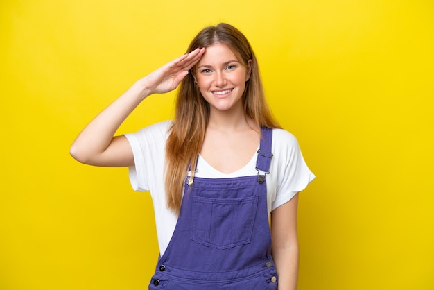 Young caucasian woman isolated on yellow background saluting with hand with happy expression