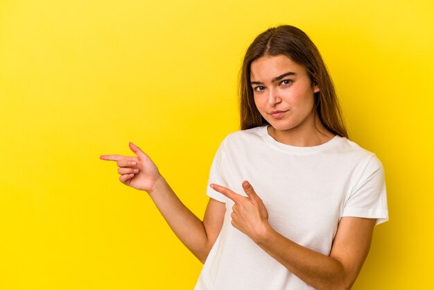 Young caucasian woman isolated on yellow background shocked pointing with index fingers to a copy space.