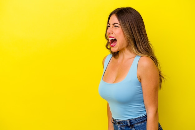 Young caucasian woman isolated on yellow background shouting very angry, rage concept, frustrated.