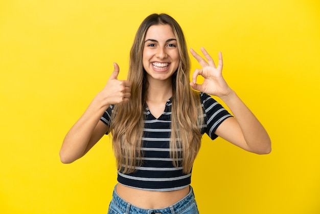 Young caucasian woman isolated on yellow background showing ok sign and thumb up gesture