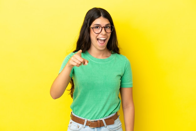 Young caucasian woman isolated on yellow background surprised and pointing front