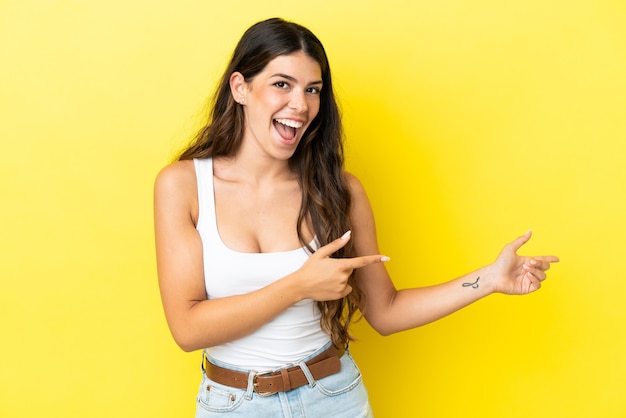 Young caucasian woman isolated on yellow background surprised and pointing side