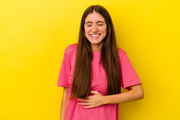 Young caucasian woman isolated on yellow background touches tummy, smiles gently, eating and satisfaction concept.