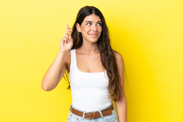 Young caucasian woman isolated on yellow background with fingers crossing and wishing the best