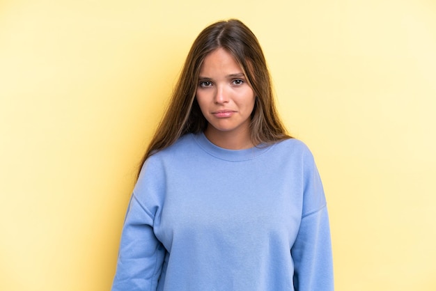 Young caucasian woman isolated on yellow background with sad expression