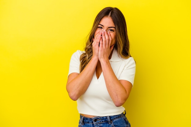 Young caucasian woman isolated on yellow wall laughing about something, covering mouth with hands.