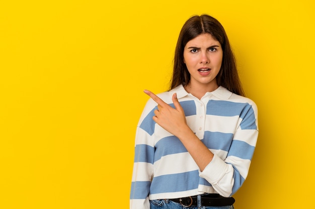 Young caucasian woman isolated on yellow wall pointing to the side