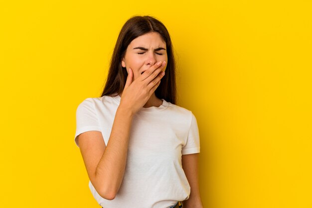 Young caucasian woman isolated on yellow wall yawning showing a tired gesture covering mouth with hand