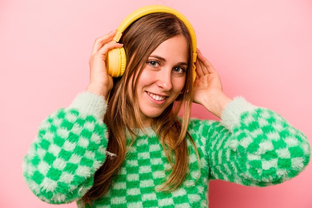 Young caucasian woman listening to music isolated on pink background