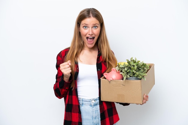 Young caucasian woman making a move while picking up a box full of things isolated on white background celebrating a victory in winner position