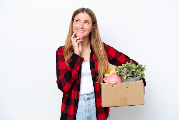 Young caucasian woman making a move while picking up a box full of things isolated on white background thinking an idea while looking up