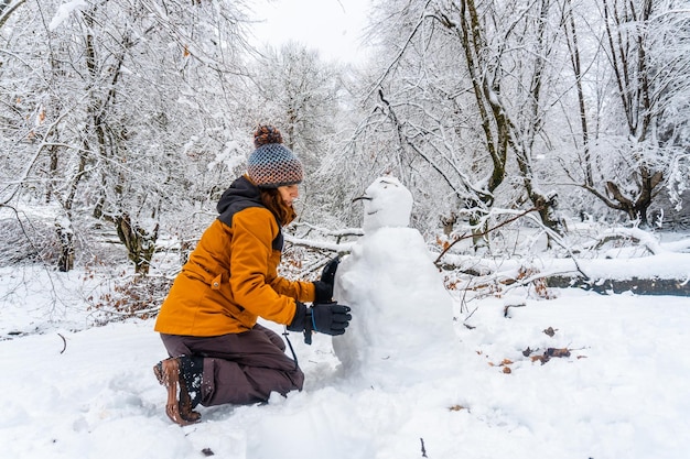 A young Caucasian woman making a snowman in the snowy forest of the Artikutza natural park in Oiartzun near San Sebastian Gipuzkoa Basque Country Spain