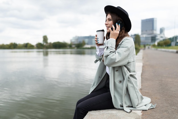 Young caucasian woman manager freelancer resting near the embankment of the river with a cup of