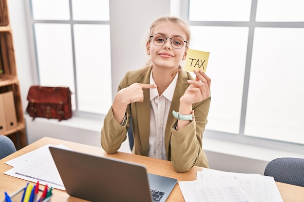 Young caucasian woman at the office calculating taxes pointing finger to one self smiling happy and proud