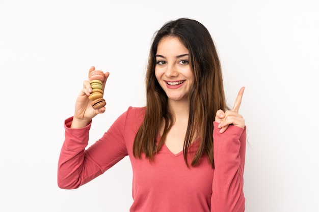 Young caucasian woman on pink wall holding colorful French macarons and pointing up a great idea