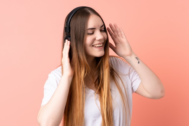 Young caucasian woman on pink wall listening music and singing