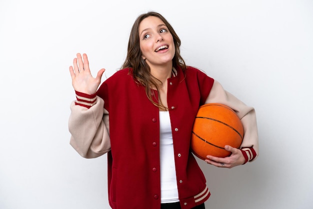 Young caucasian woman playing basketball isolated on white background saluting with hand with happy expression