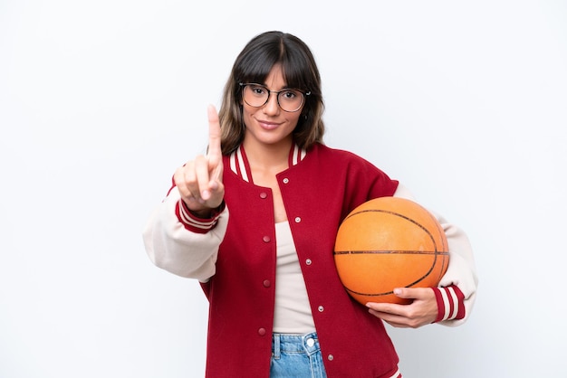 Young caucasian woman playing basketball isolated on white background showing and lifting a finger