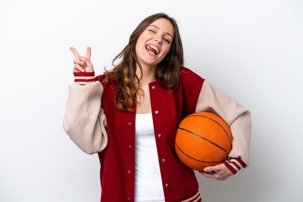 Young caucasian woman playing basketball isolated on white background smiling and showing victory sign