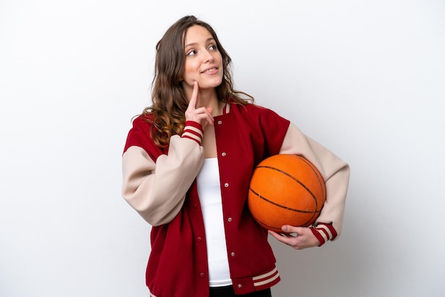 Young caucasian woman playing basketball isolated on white background thinking an idea while looking up