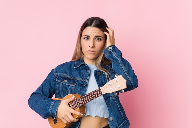 Young caucasian woman playing ukelele being shocked, she has remembered important meeting.