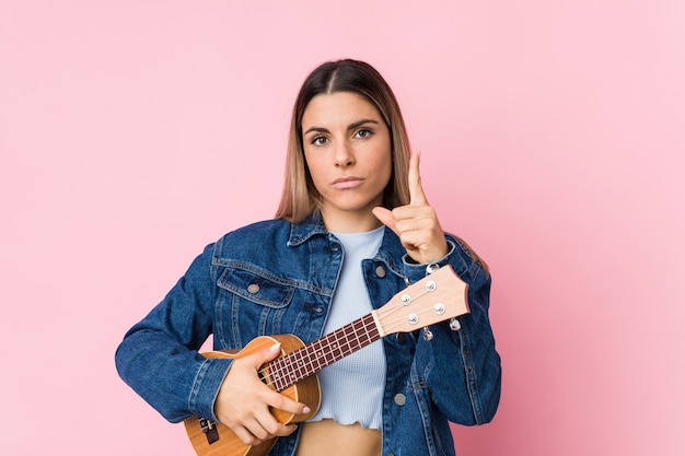 Young caucasian woman playing ukelele showing number one with finger.