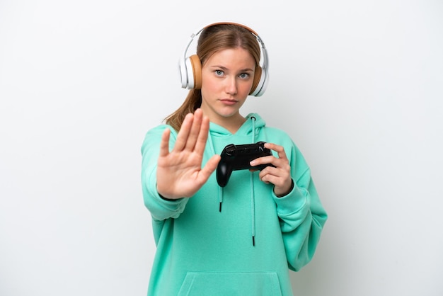 Young caucasian woman playing with a video game controller isolated on white background making stop gesture