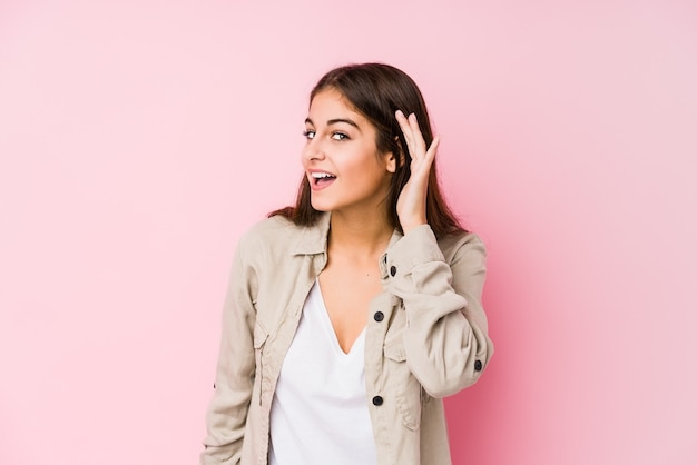 Young caucasian woman posing in a pink  trying to listening a gossip.