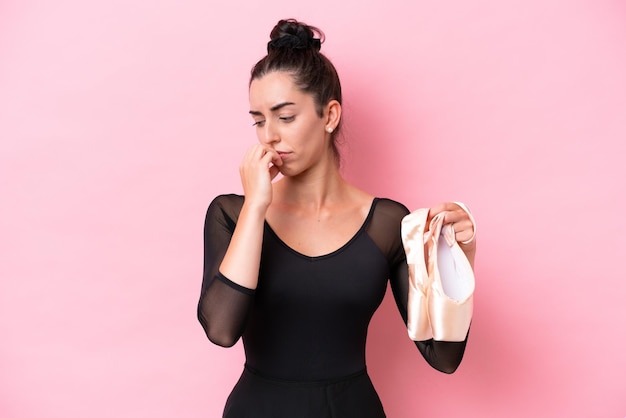 Young caucasian woman practicing ballet isolated on pink background having doubts