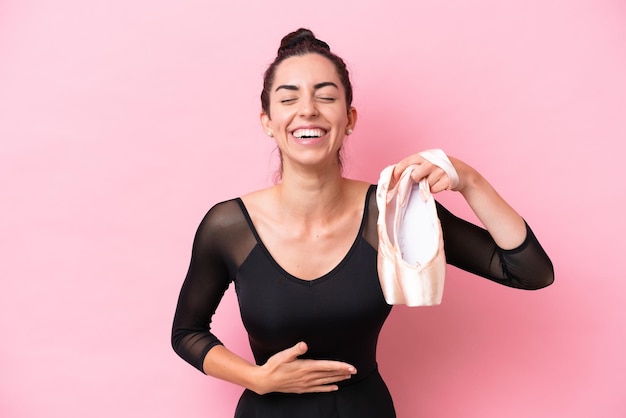 Young caucasian woman practicing ballet isolated on pink background smiling a lot