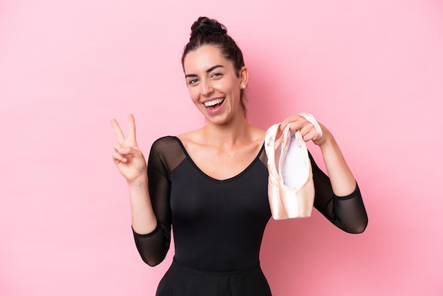 Young caucasian woman practicing ballet isolated on pink background smiling and showing victory sign