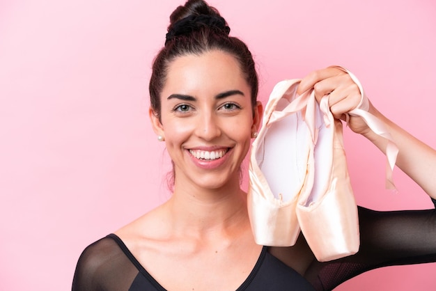 Young caucasian woman practicing ballet isolated on pink background