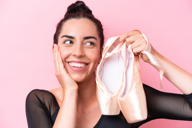 Young caucasian woman practicing ballet isolated on pink background