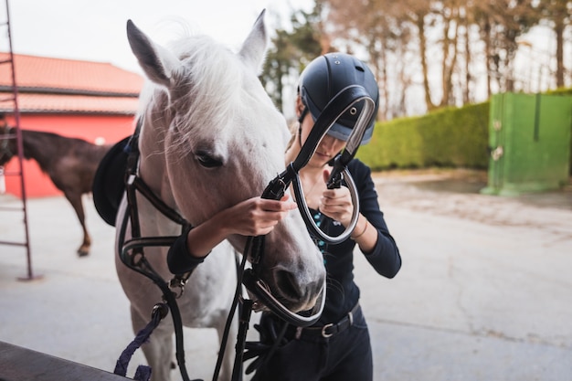 Young caucasian woman preparing a white horse for a ride