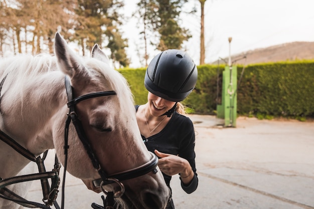 Young caucasian woman preparing a white horse for a ride