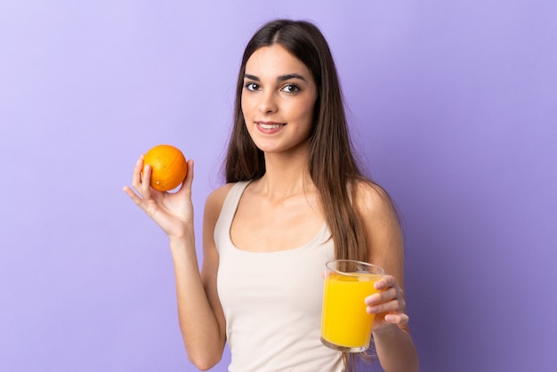 Young caucasian woman on purple holding an orange and an orange juice