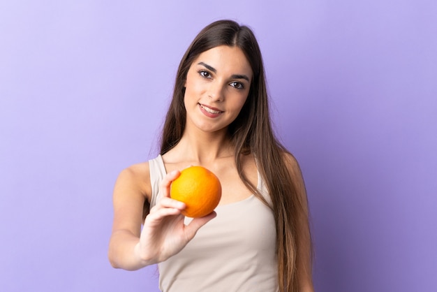 Young caucasian woman on purple holding an orange