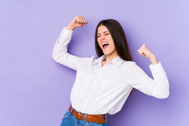 Young caucasian woman on purple wall raising fist after a victory