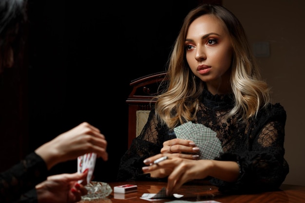 Young caucasian woman sits at a table plays cards for undressing and smokes