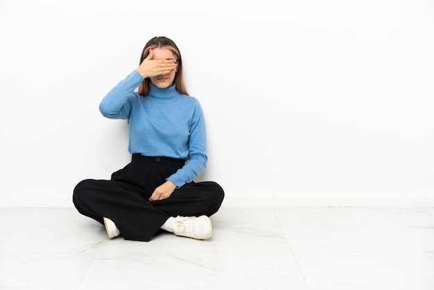 Young Caucasian woman sitting on the floor covering eyes by hands. Do not want to see something