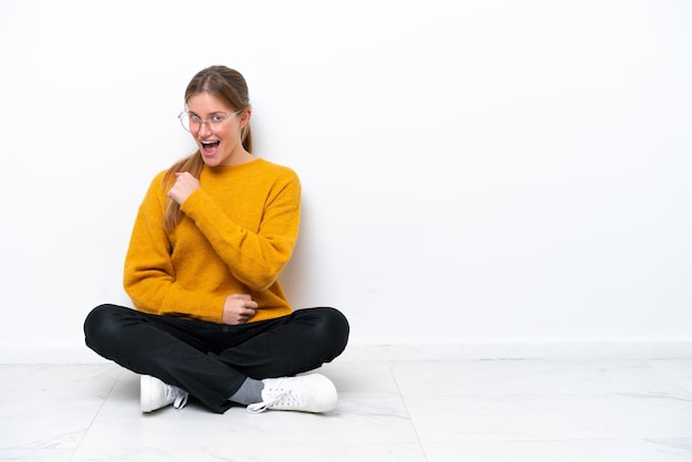 Young caucasian woman sitting on the floor isolated on white background celebrating a victory