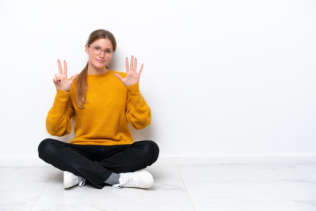 Young caucasian woman sitting on the floor isolated on white background counting eight with fingers