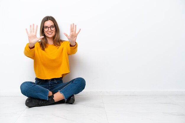 Young caucasian woman sitting on the floor isolated on white background counting ten with fingers